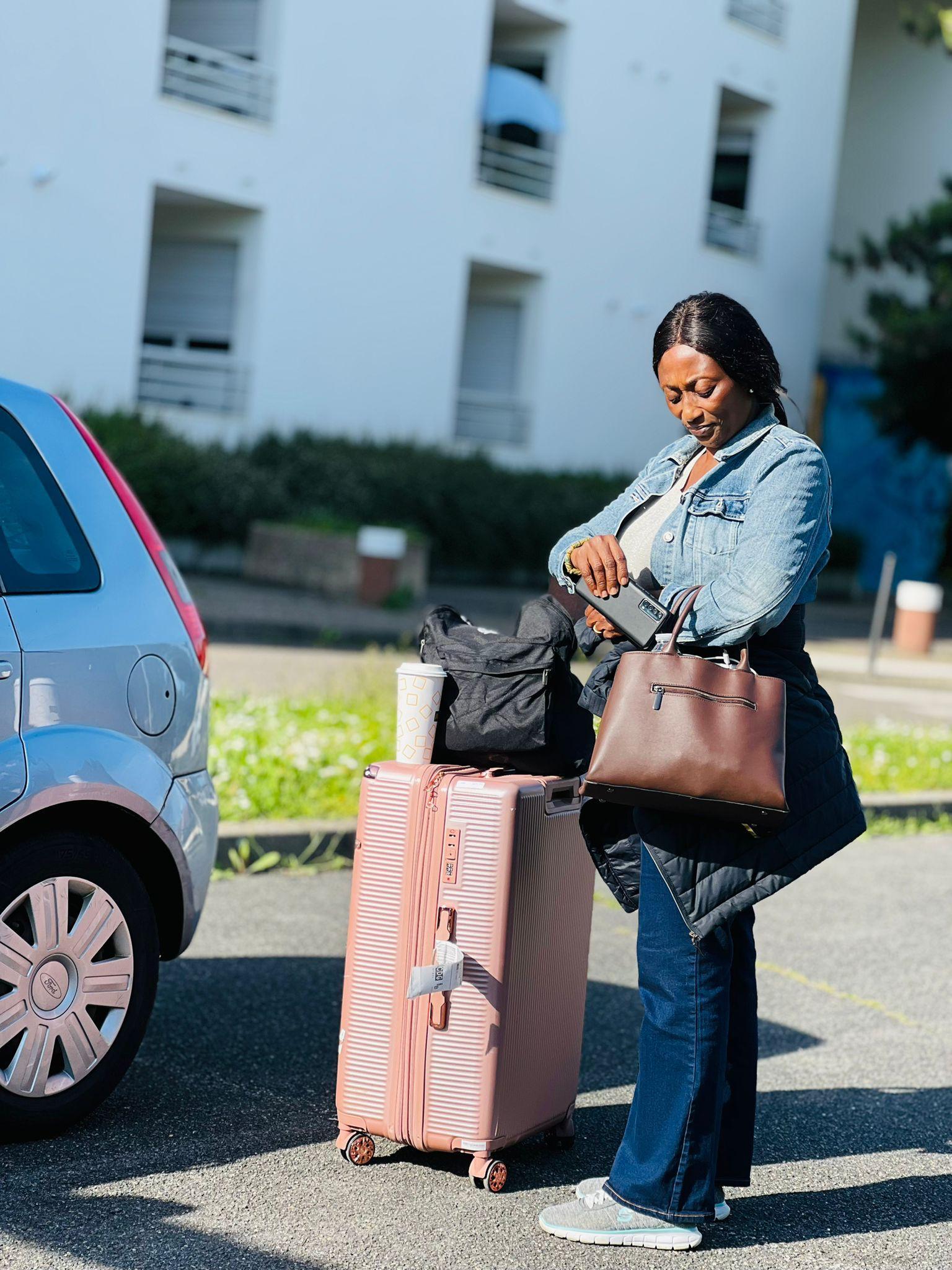 A traveller arriving at her door with her suitcase beside the car